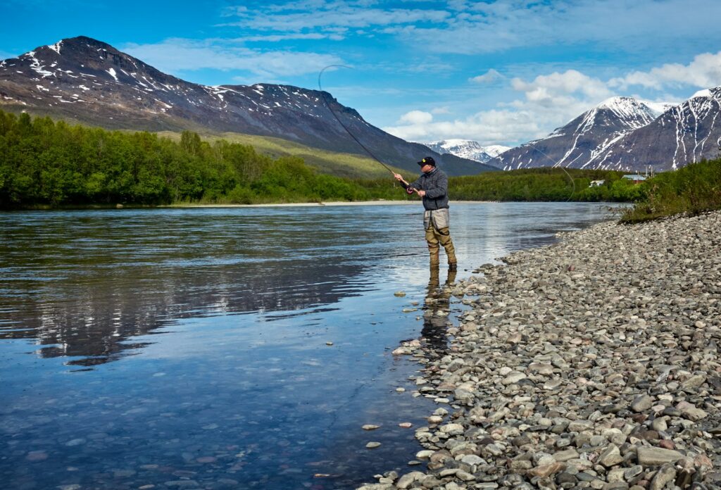 A man fishing on a wide river in evening light